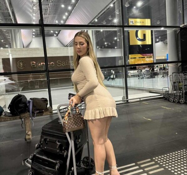 Influenciadora Malévola Alves sorrindo no aeroporto do Egito após liberação, com mala de viagem