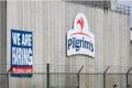 Logotipo da JBS e Pilgrim's Pride sobre fundo de fábrica de processamento de carne, simbolizando aquisição