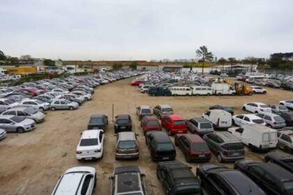 Fileira de veículos oficiais do Governo de SP em leilão, carros e motos estacionados em pátio aberto