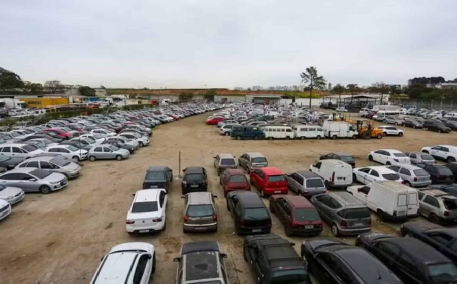 Fileira de veículos oficiais do Governo de SP em leilão, carros e motos estacionados em pátio aberto