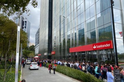 Sede do Santander Brasil com gráfico de ações em queda representando lucro 28% menor