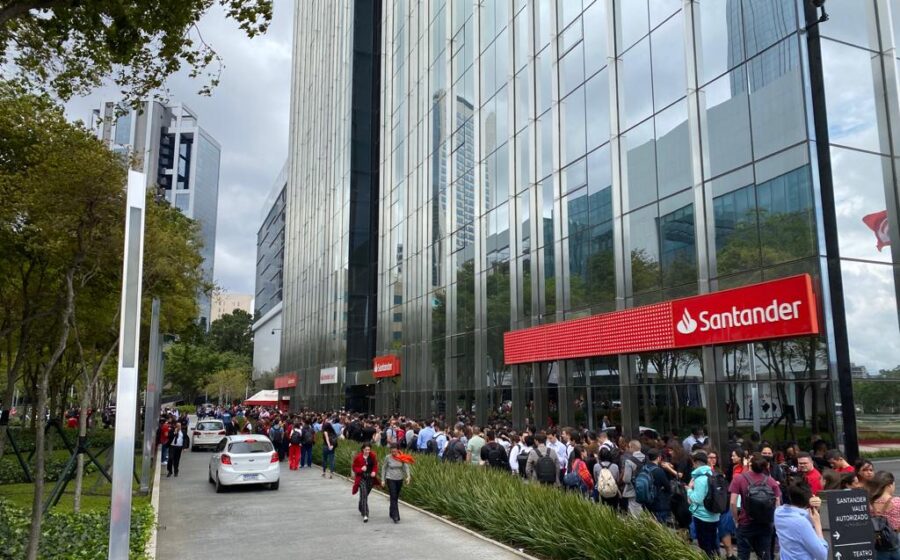 Sede do Santander Brasil com gráfico de ações em queda representando lucro 28% menor