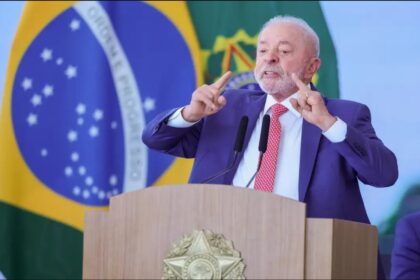 Lula discursa após vitória eleitoral com logos de Big Techs ao fundo simbolizando regulação