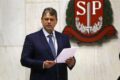 Governador segurando celular diante de rodovia esburacada e obras paralisadas