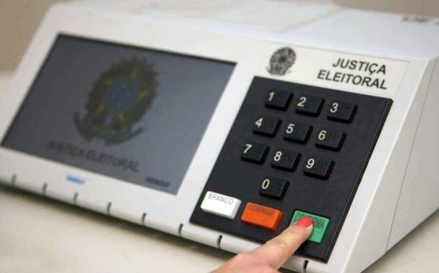 urna eletrônica sendo auditada por oficiais em mesa de votação com lacres e documentos