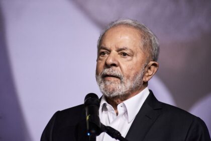 Lula discursa com gráficos de dívida pública e juros ao fundo, símbolo de desafio fiscal