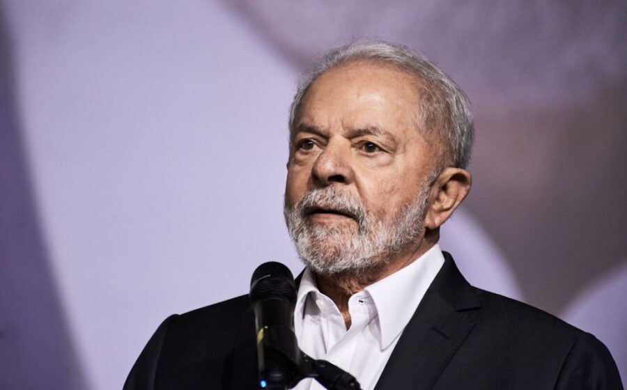 Lula discursa com gráficos de dívida pública e juros ao fundo, símbolo de desafio fiscal