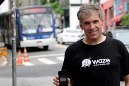 Uri Levine, cofundador do Waze, sorri em evento no Brasil com bandeira brasileira ao fundo