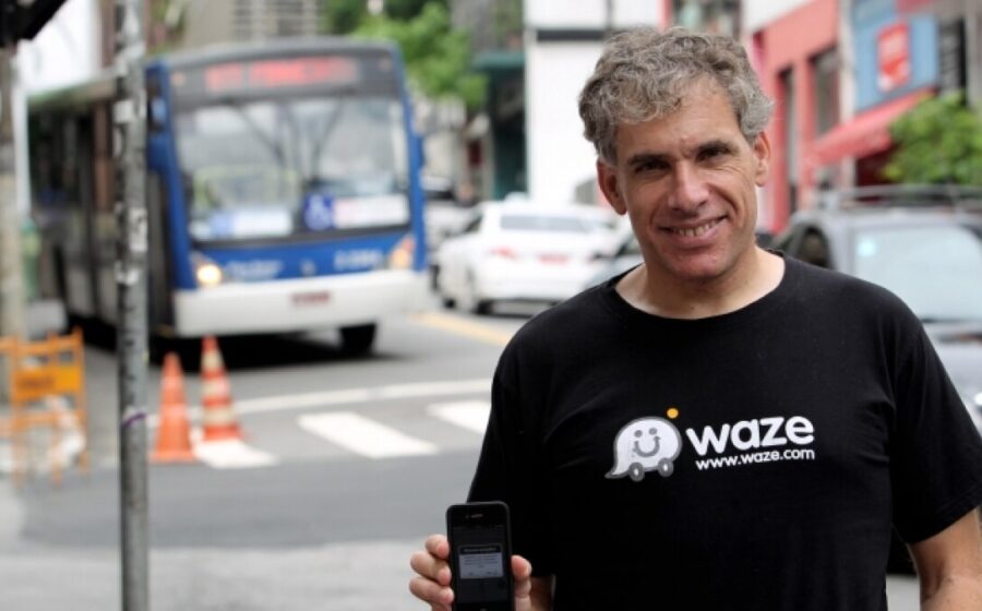 Uri Levine, cofundador do Waze, sorri em evento no Brasil com bandeira brasileira ao fundo