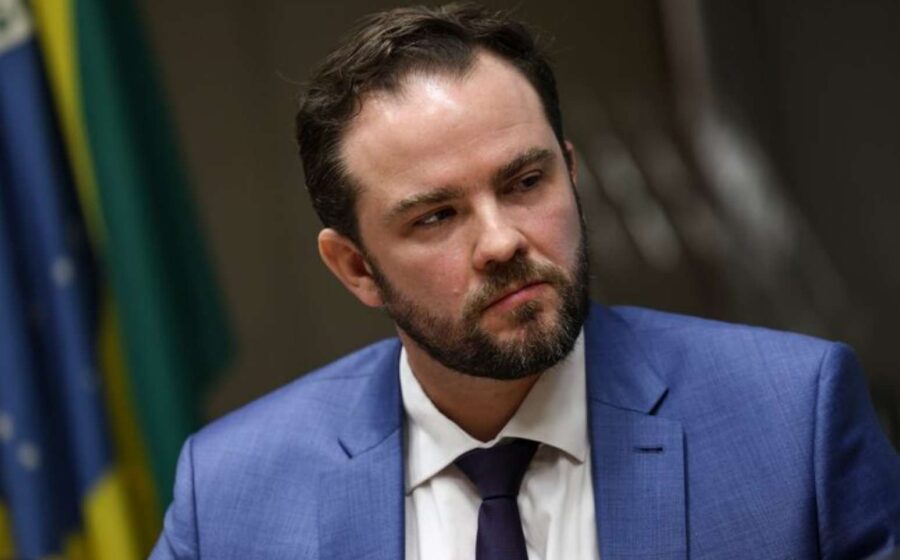 Silhueta de ministro da Fazenda sobre gráficos econômicos e bandeira do Brasil
