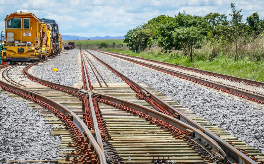 Trilhos de ferrovia brasileira paralisados com composição de cargas parada sob céu nublado