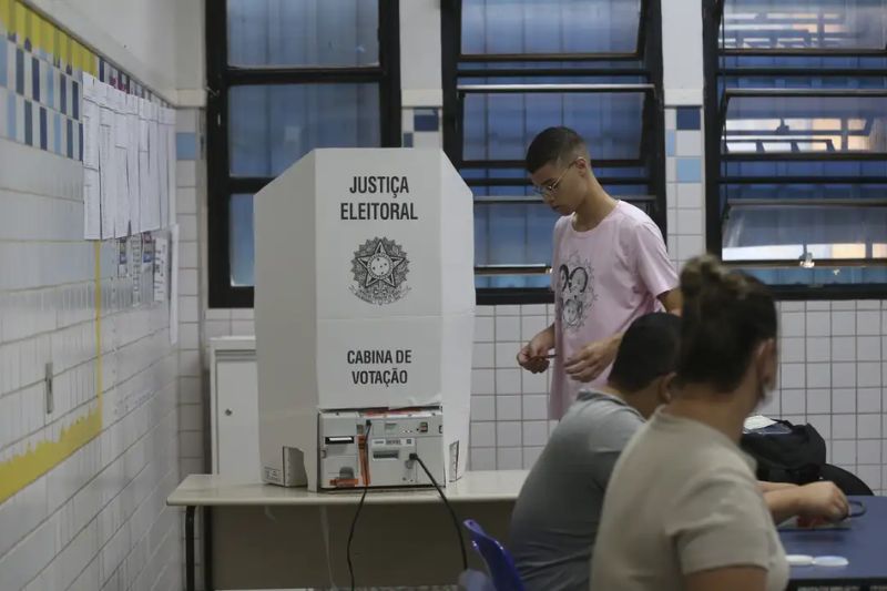 Eleitores em fila para votar no segundo turno em Minas Gerais, urna eletrônica em destaque