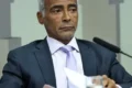 Senador Flávio Bolsonaro com bandeira dos EUA e símbolo de salário cortado, representando fuga e ação judicial