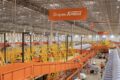 Centro de distribuição Shopee com esteiras transportadoras e pacotes laranja, simbolizando expansão logística de 60% no Brasil