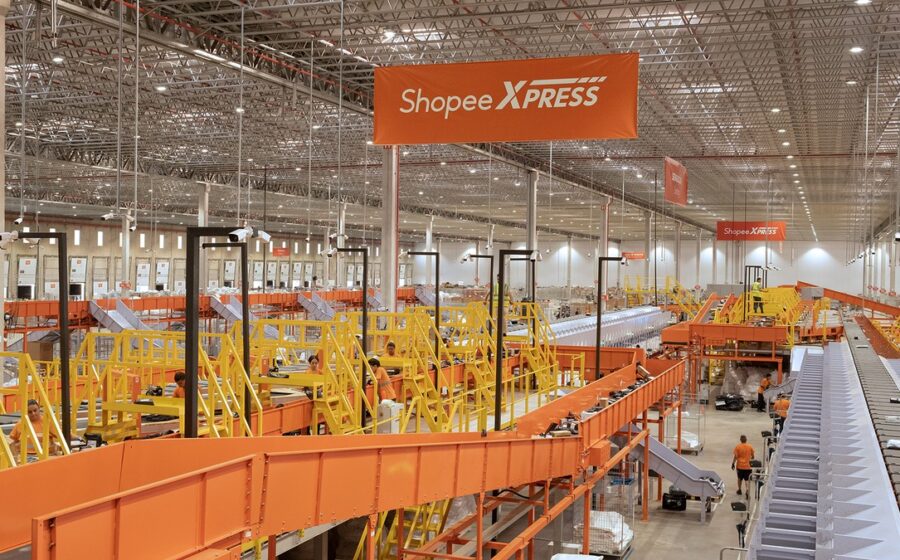 Centro de distribuição Shopee com esteiras transportadoras e pacotes laranja, simbolizando expansão logística de 60% no Brasil
